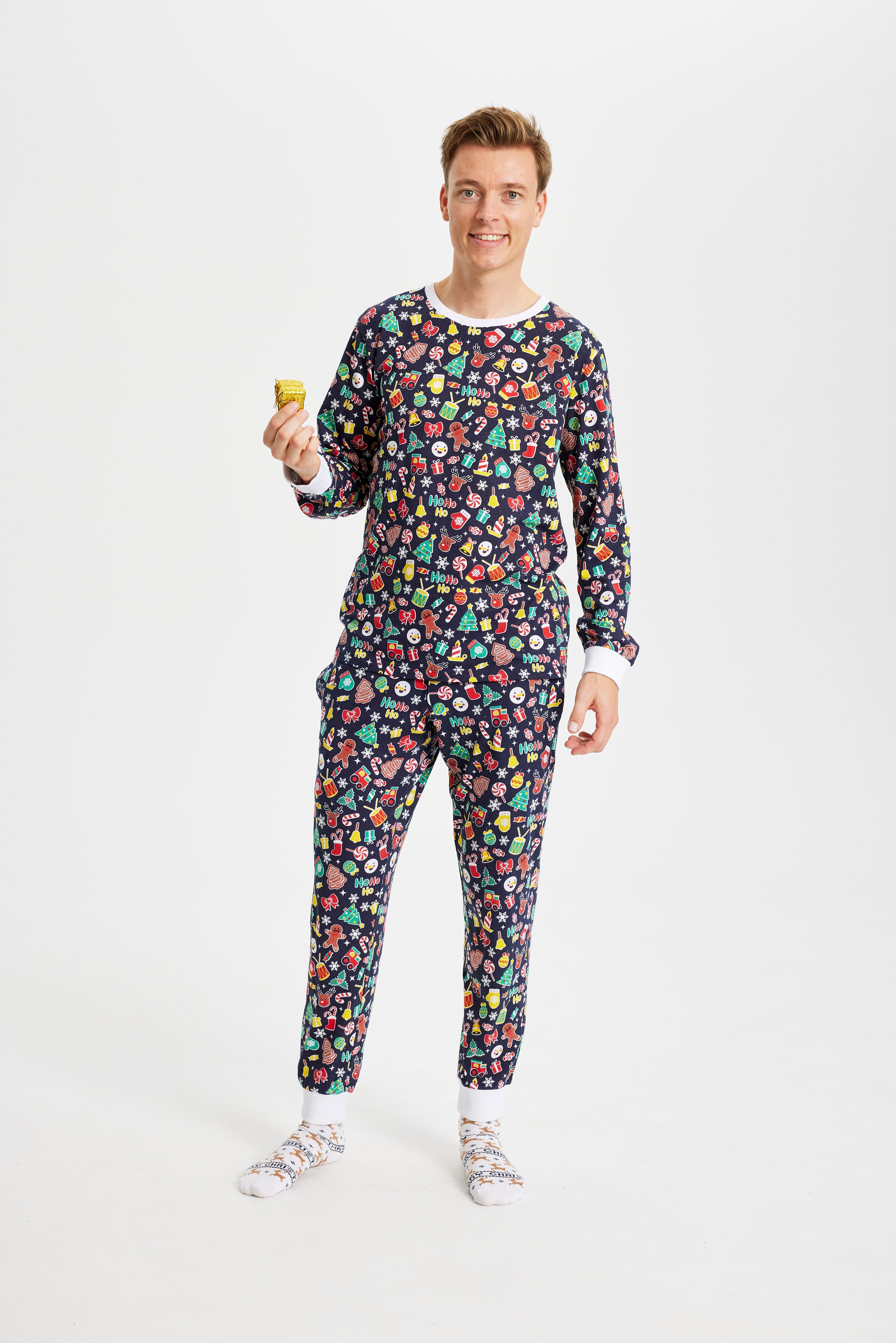 En mand smiler, mens han er iført en blå julepyjamas med juletræer, klokker og vanter på.